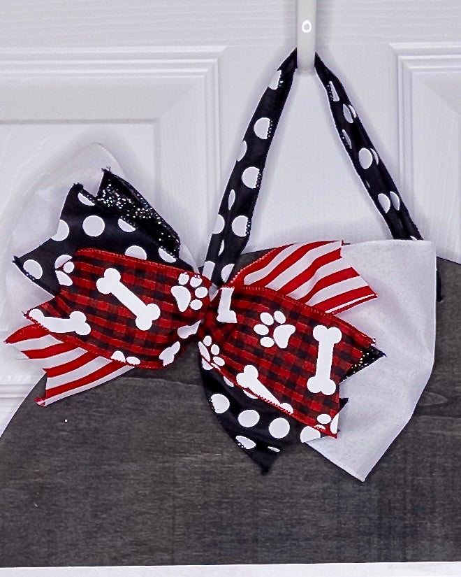 Dog bandana with a large bow featuring red, white, and black patterns on a gray surface.