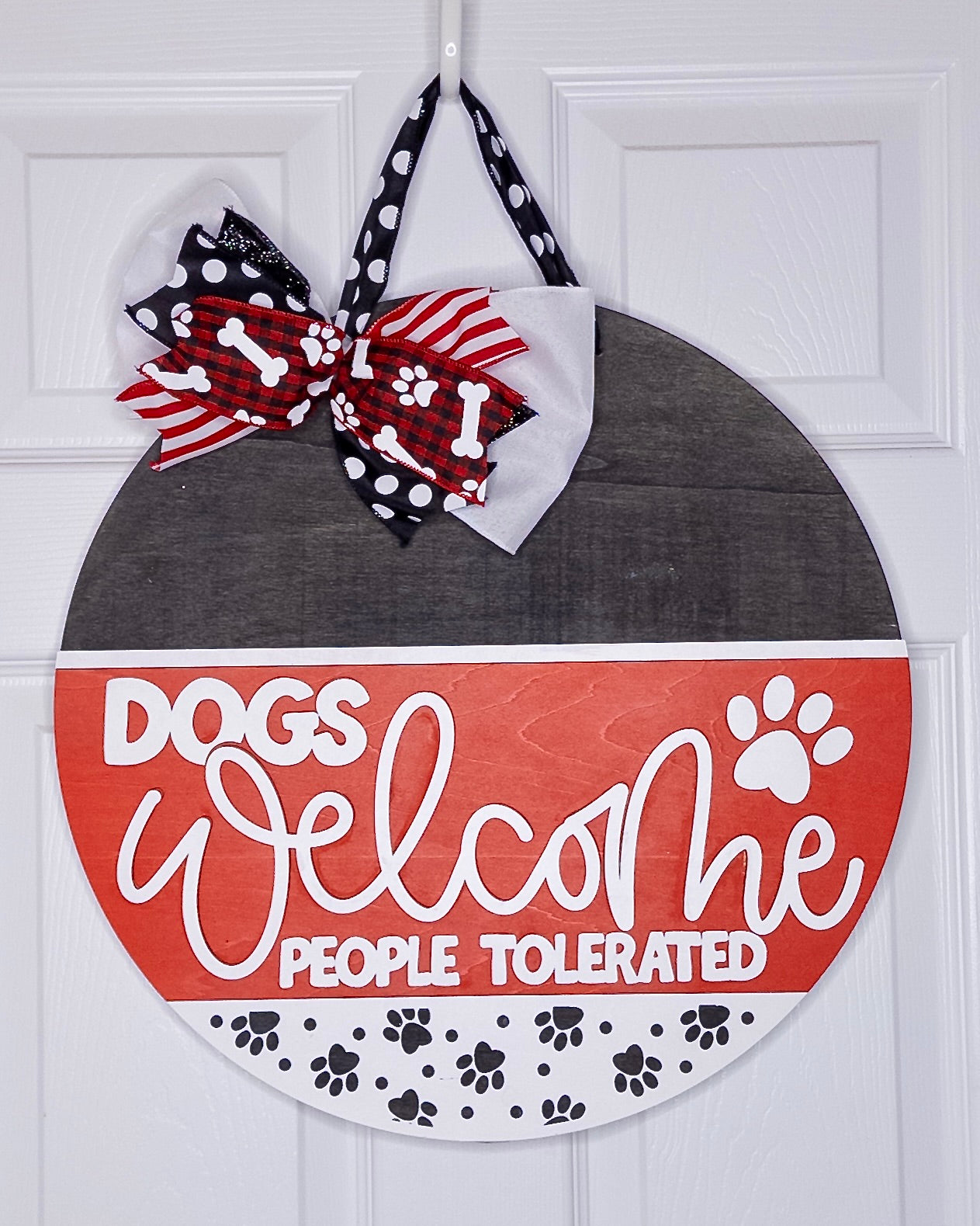 Decorative door hanger with 'Dogs Welcome, People Tolerated' text and bows on a white background