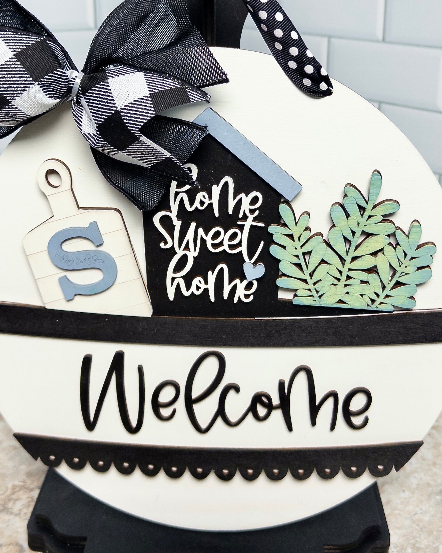 Decorative sign with 'Home Sweet Home' and 'Welcome' text, featuring a black and white checkered ribbon.