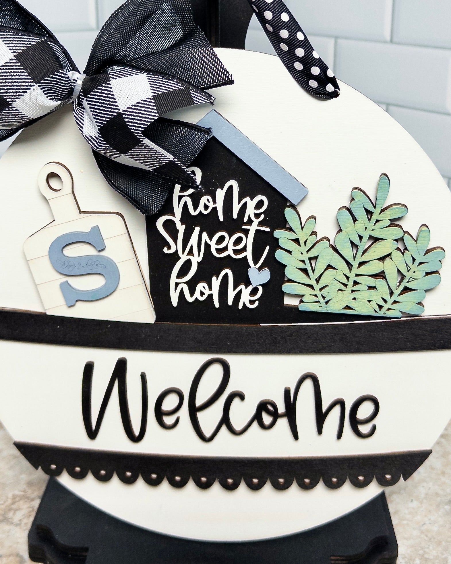 Decorative sign with 'Home Sweet Home' and 'Welcome' text, featuring a black and white checkered ribbon.
