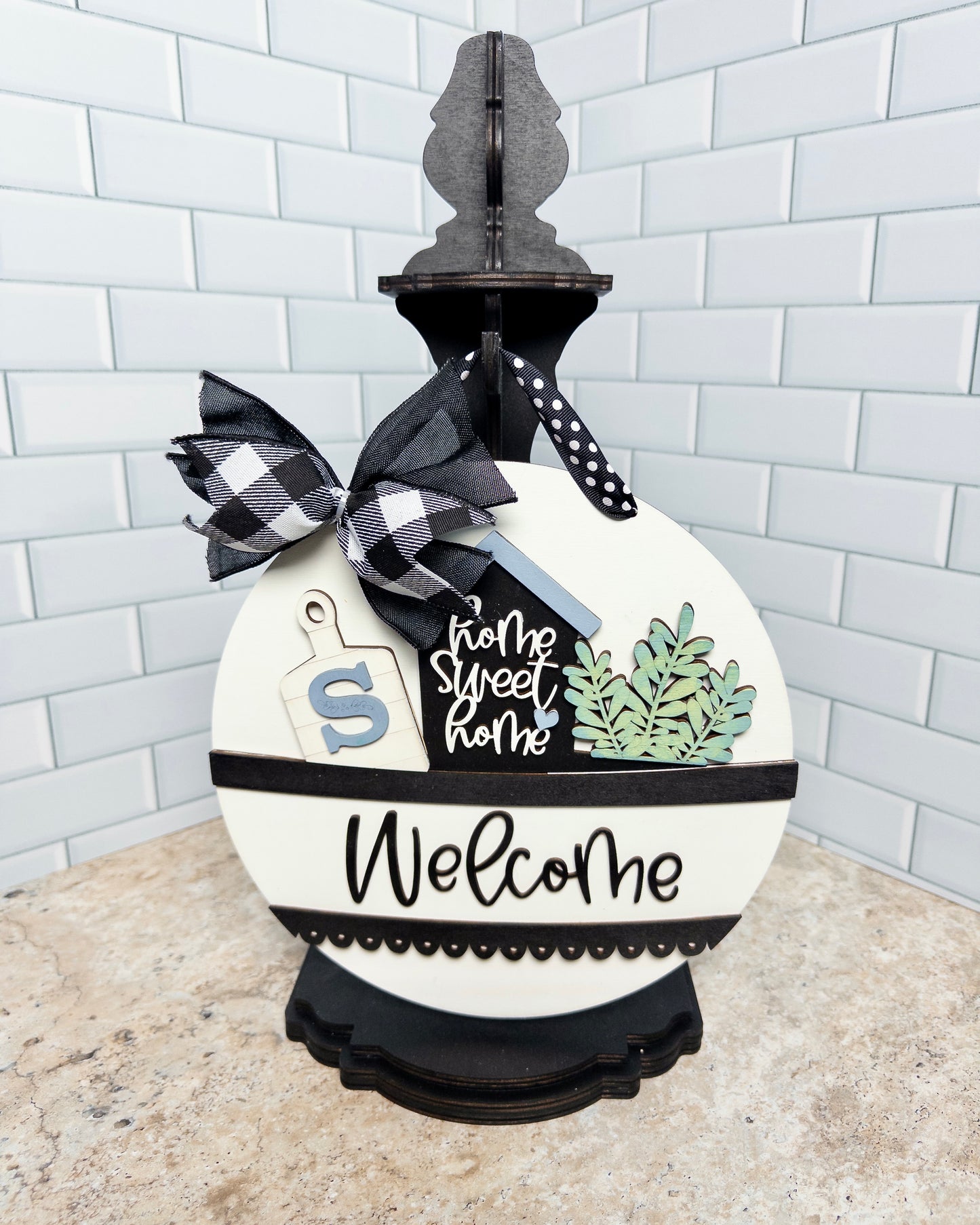 Decorative sign with 'home sweet home' and 'Welcome' text, featuring a checkered bow on a white background.