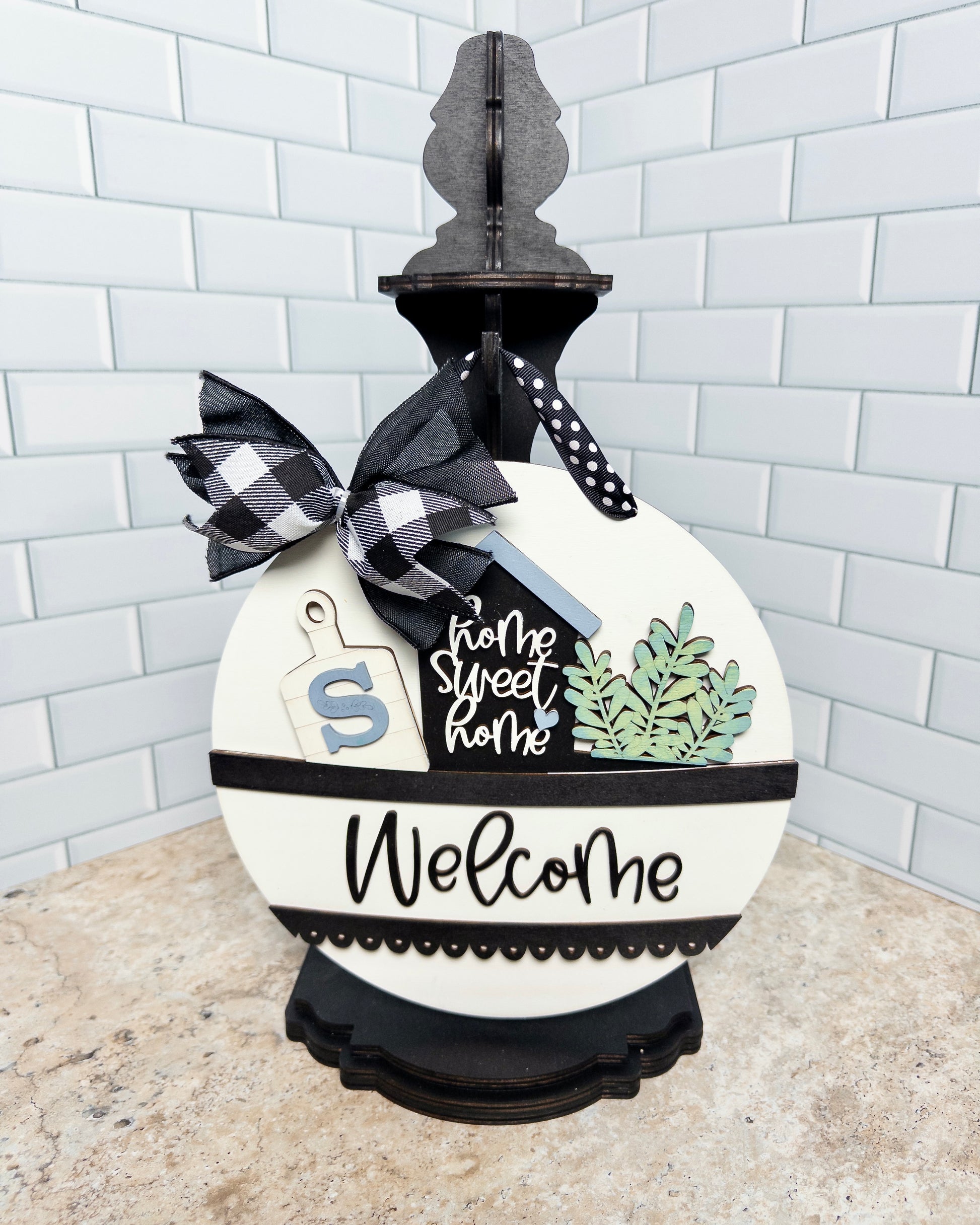 Decorative sign with 'home sweet home' and 'Welcome' text, featuring a checkered bow on a white background.