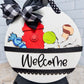 Decorative sign with cartoon characters and 'Welcome' text, featuring a black and white checkered bow.