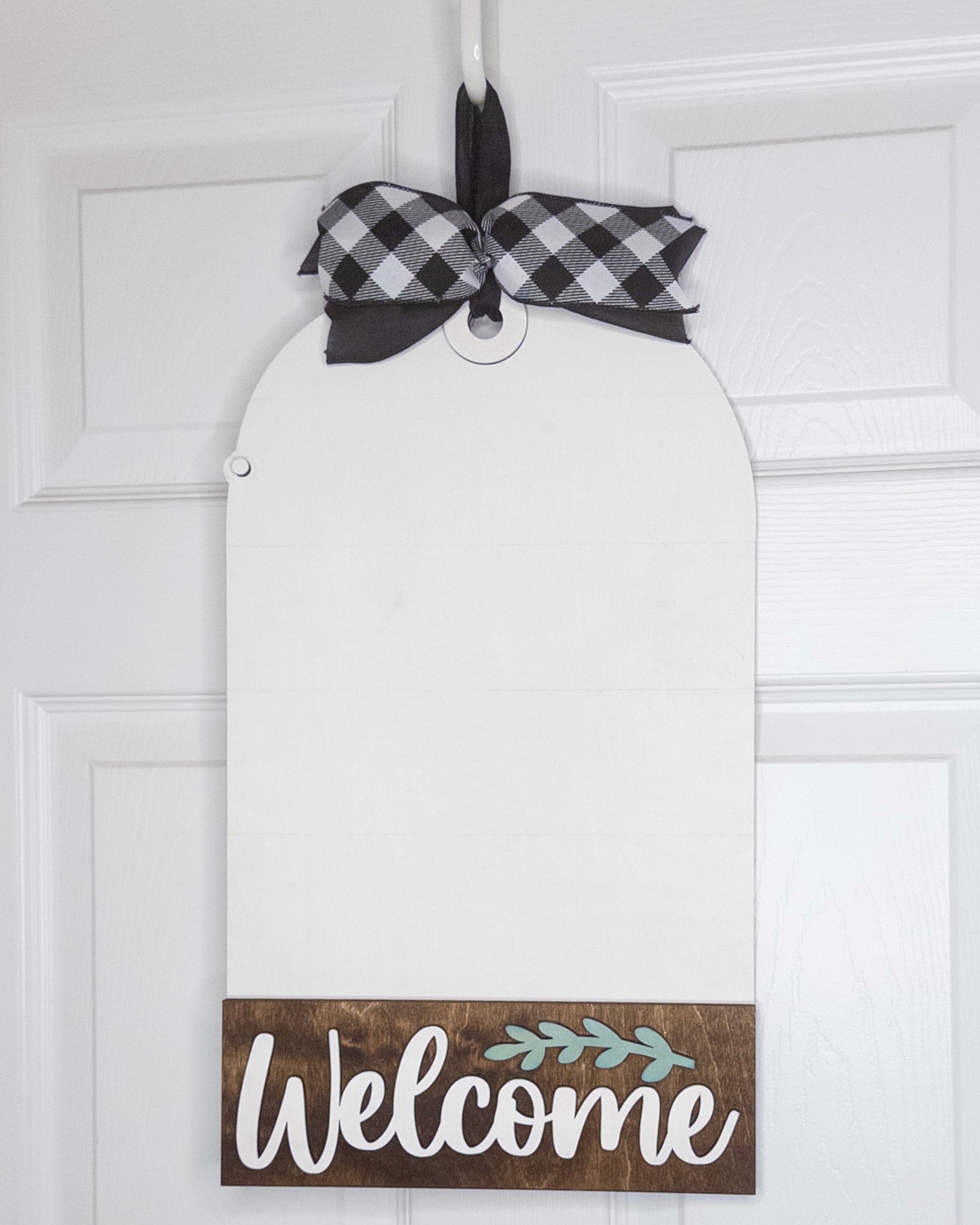 Decorative door hanger with 'Welcome' sign and plaid ribbon on a white door.