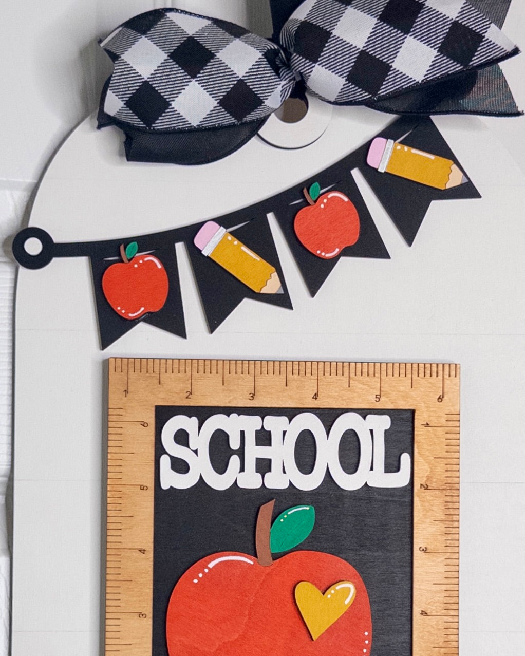 Decorative school-themed item with apple, pencil, and banner design on a white background.
