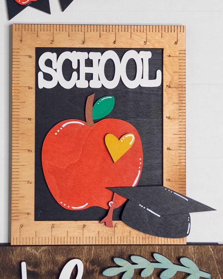 Decorative sign with an apple, heart, and 'SCHOOL' text on a wooden frame.