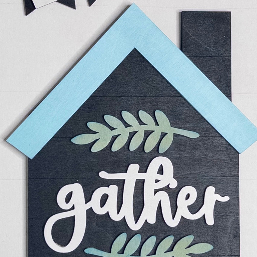 Decorative sign with 'gather' text and leaf designs on a blue and gray background