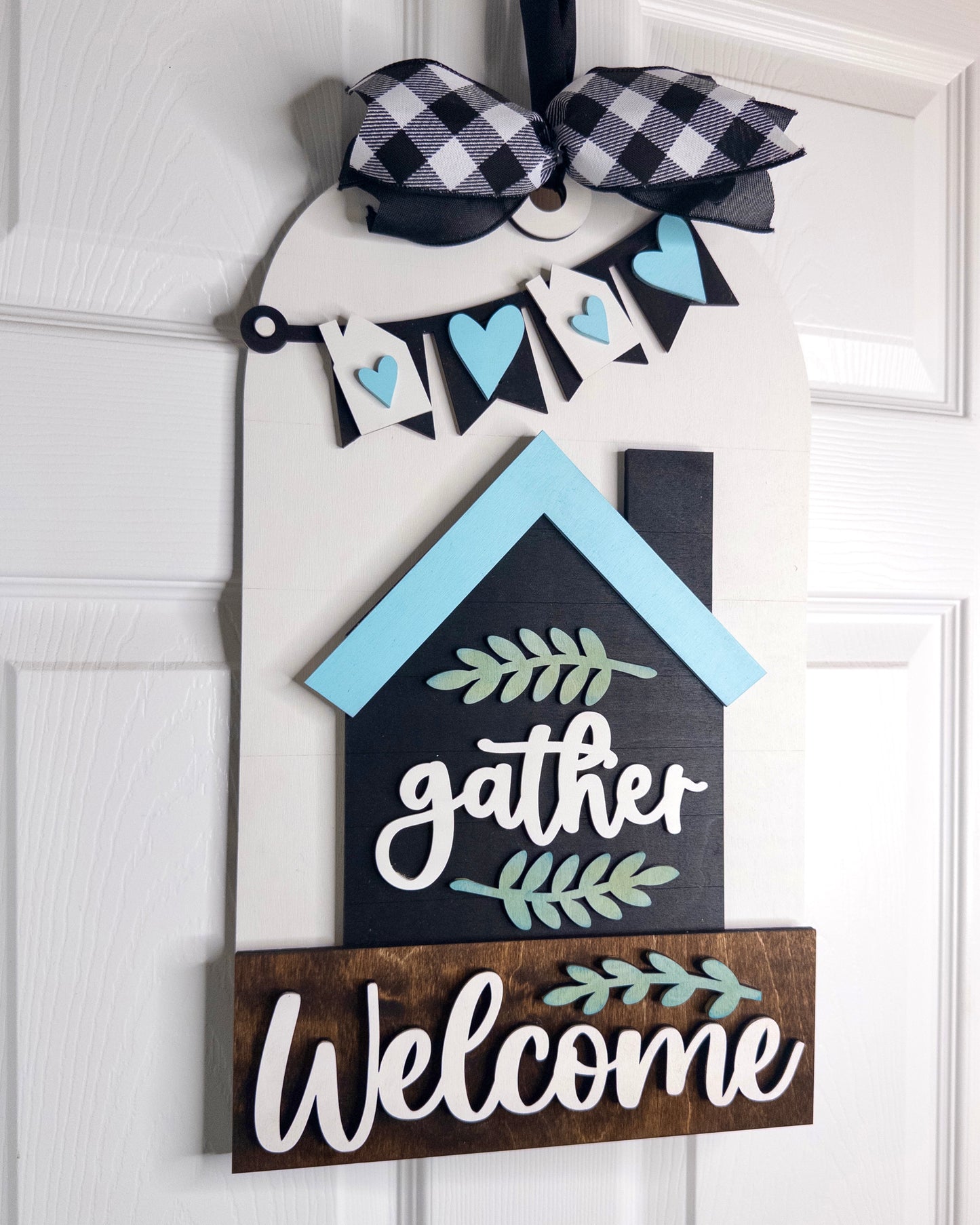 Decorative door hanger with 'gather' and 'Welcome' text on a white door.