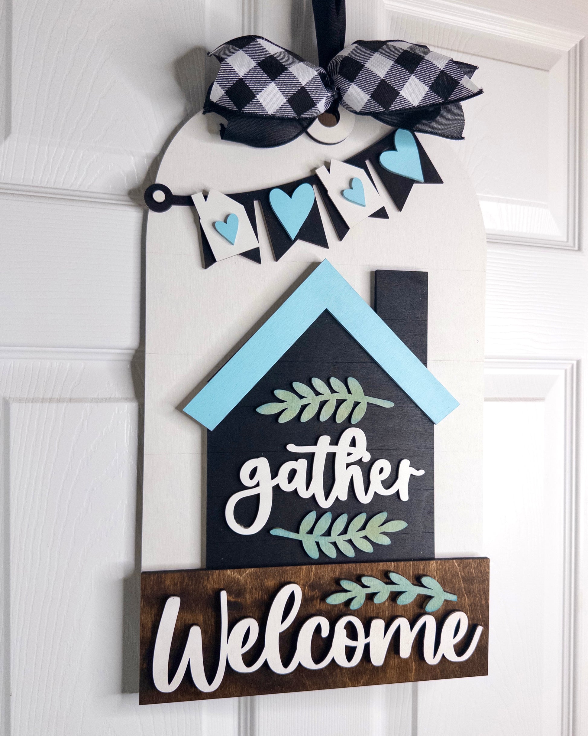 Decorative door hanger with 'gather' and 'Welcome' text on a white door.