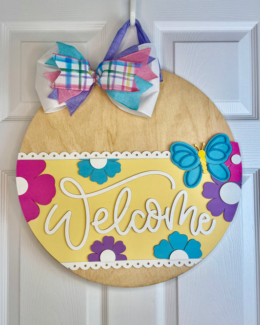 Decorative door hanger with colorful flowers and a bow on a white door.