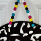 Colorful beaded necklace on a black and white patterned stand against a white background